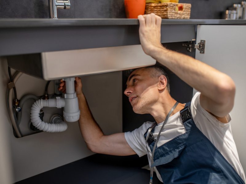Man carefully examining bottom of sink and pipe